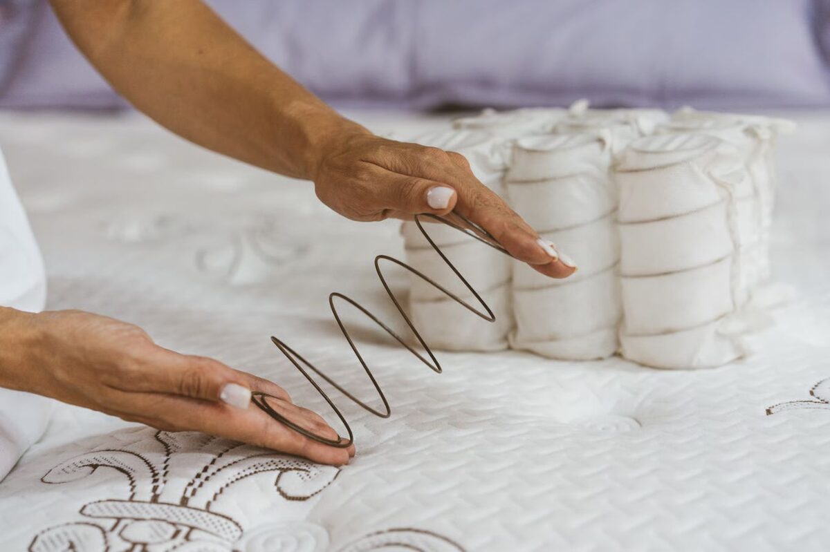 Két kéz egy homokóra alakú fémrugót tart textilzsákos rugóegységek előtt